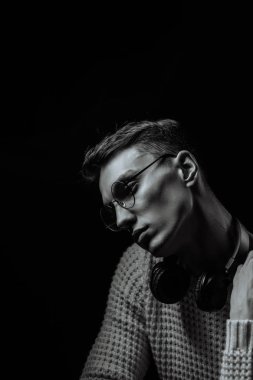 Gözlüklü ve kulaklıklı genç adam siyah arka planda müzik dinliyor.