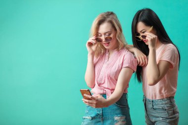 Mutlu genç kızlar mavi duvara karşı akıllı telefonlarıyla selfie çekiyorlar.