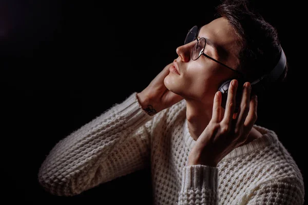 Młody człowiek w okularach i słuchawkach słuchający muzyki na czarnym tle — Zdjęcie stockowe
