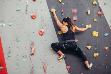 Genç dağcı kadın tırmanış merkezinde pratik kayalara tırmanıyor, kaya tırmanıyor.