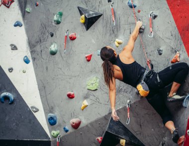 Sporcu kız spor salonundaki kaya tırmanışı duvarına tırmanıyor.