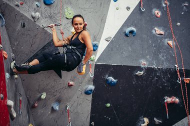 Sporcu kız spor salonundaki kaya tırmanışı duvarına tırmanıyor.