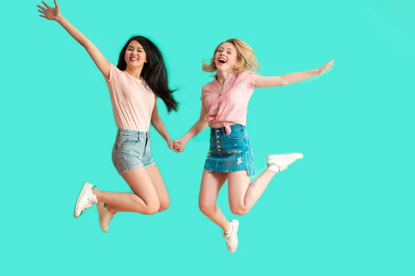 Δύο χαρούμενες ανέμελες νεαρές γυναίκες που πηδάνε πάνω από μπλε φόντο — Φωτογραφία Αρχείου