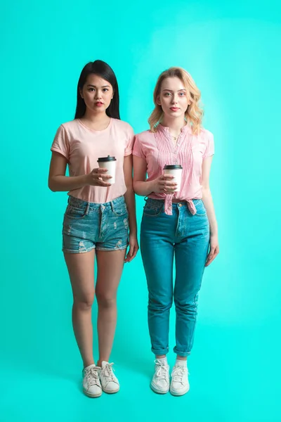 Két multiracionális lány kávéval a kezében, elszigetelve a kék felett. — Stock Fotó