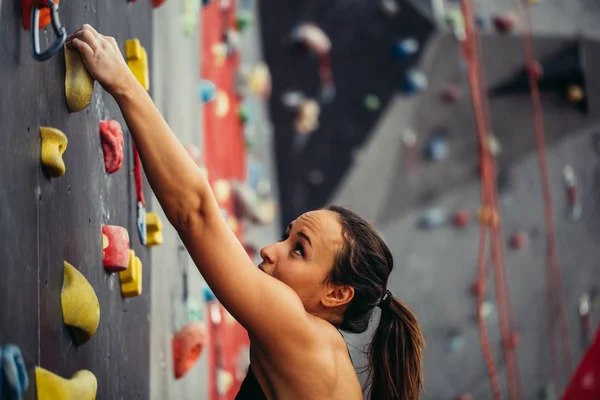 Sportliche junge Frau trainiert in einer bunten Kletterhalle. — Stockfoto