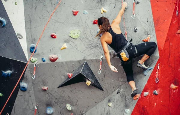 Sportliche junge Frau beim Training in einer bunten Kletterhalle. Freiklettererin klettert drinnen hoch — Stockfoto