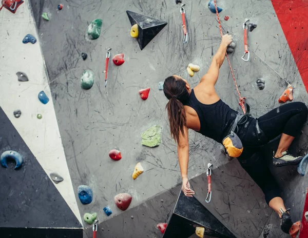 Sporcu kız spor salonundaki kaya tırmanışı duvarına tırmanıyor.