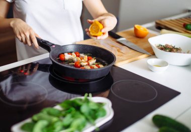 Genç ve mutlu ev kadınının akşam yemeği için tavuk eti kızartışı görüntüsü.