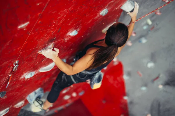 Schöne junge starke Frau klettert auf rote künstliche Wand Draufsicht. — Stockfoto