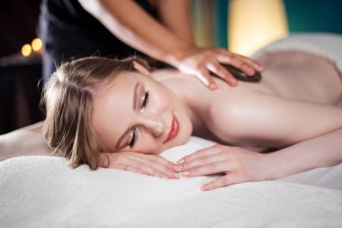 Güzel, genç ve sağlıklı bir kadın sıcak taş masajı yaptırıyor. Spa Tedavisi