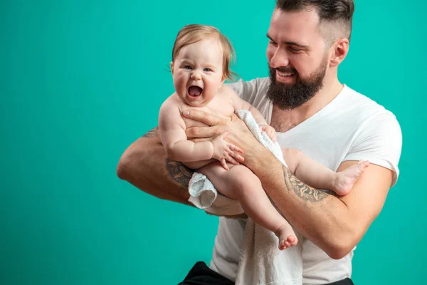 Pai brincalhão carregando seu filho bebê sorridente no pescoço sobre fundo azul — Fotografia de Stock