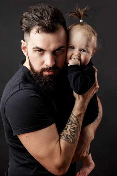 Knappe getatoeëerd jonge man houdt van schattige kleine baby op zwarte achtergrond — Stockfoto