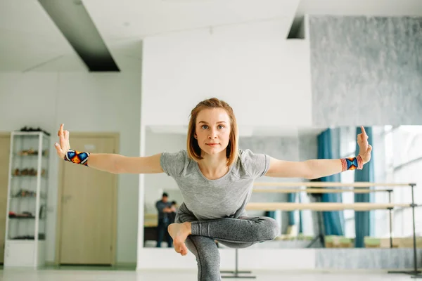 Женщина делает упражнения балансировки во время тренировки йоги в хорошо освещенном спортзале — стоковое фото