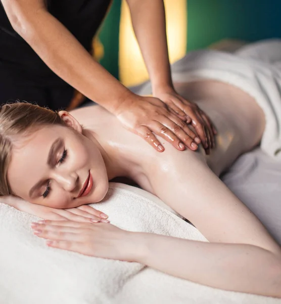 Jovem tendo prazer na cama de massagem, com os olhos fechados. Mulher. Salão de Spa. — Fotografia de Stock