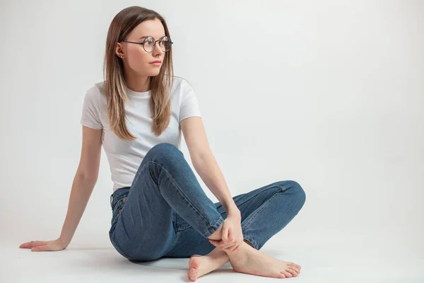 Продумана молода дівчина в окулярах сидить на підлозі — стокове фото