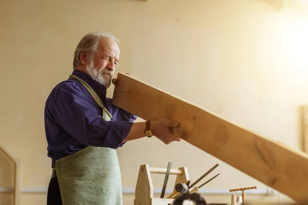 Старый красивый столярщик измеряет доску в мастерской. — стоковое фото
