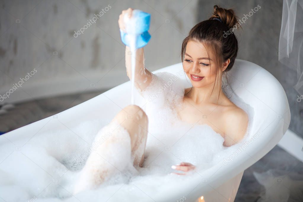 happy model putting foam on her legs in modern bathroom