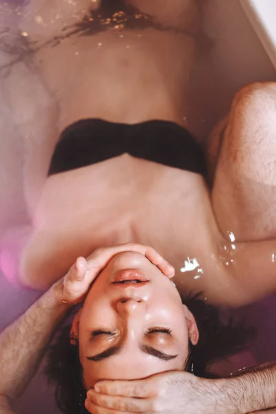 Мужчина учит женщину плавать на спине в джакузи — стоковое фото