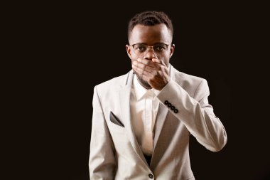 Genç Afro adam ağzını koyu arka plan üzerinde eliyle kapalı tutmak.