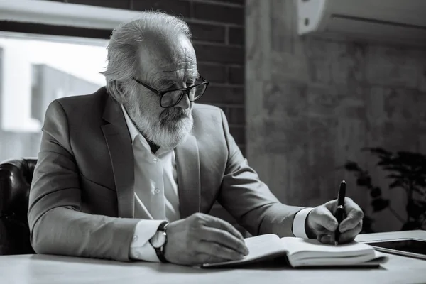 Zwart / wit foto. Senior man holding pen en schrijven in notitieblok — Stockfoto