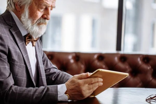 Pensionista en traje gris está mirando las fotos en la tableta — Foto de Stock