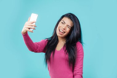 beautiful winking girl posing to her smartphone to take a photo clipart