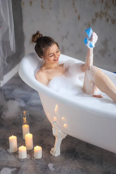 Приємна дівчина розміщує губкою у ванній зі свічками на підлозі — стокове фото