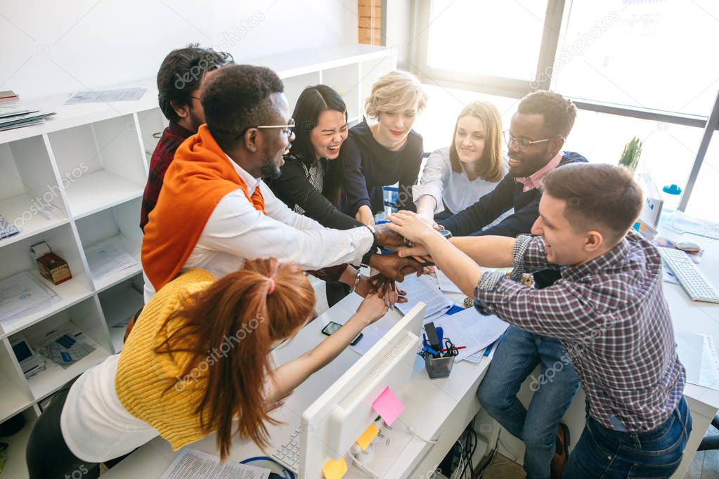 Creative happy multinational business team putting hands together at the office