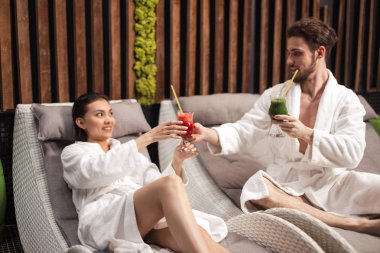 Suyu gözlük tutan ve beldesinde oturan çekici çift. Yakışıklı adam kadına kokteyl veriyor. Tatil romantik