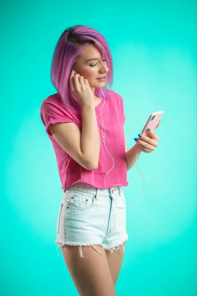 Señora de pelo rosa escuchando música en auriculares sobre fondo azul . — Foto de Stock