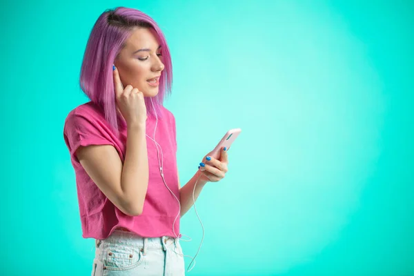 Señora de pelo rosa escuchando música en auriculares sobre fondo azul . — Foto de Stock