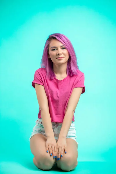 bright young beautiful girl with pink colored hair sitting on the floor