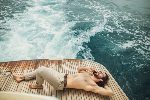 Mann entspannt sich in der Sonne, auf einem Boot auf dem Meer liegend. Luxusurlaub auf einer Jacht auf den Inseln. — Stockfoto