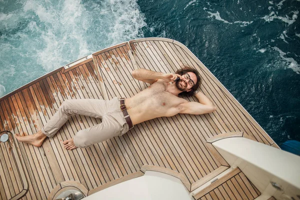 Homem relaxando sob o sol, deitado em um barco no mar. Férias de luxo em um iate nas ilhas. — Fotografia de Stock