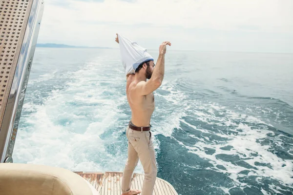 Rückansicht eines jungen Mannes, der am Rand der Jacht sitzt und aufs Meer blickt — Stockfoto