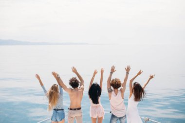 Okyanustaki yelkenlide kutlama yapan arkadaşların arka görüntüsü, kollar havada..