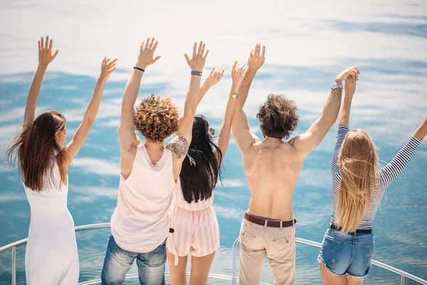 Widok z tyłu przyjaciół świętować na żaglówce w oceanie, ramiona podniesione. — Zdjęcie stockowe