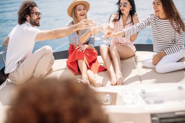 Mutlu arkadaşlar şampanya bardaklarını tokuşturup yatta yelken açıyorlar.