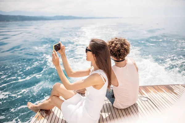 Young photographer taking picture of his girlfriend on seaboat — Stock Photo, Image
