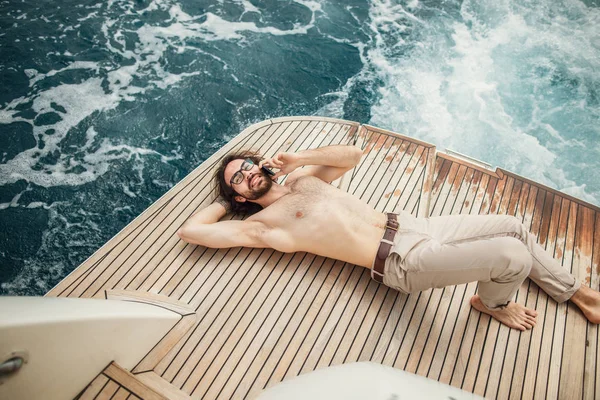 Человек отдыхает под солнцем, лежа на лодке в море. Роскошный отдых на яхте на островах. — стоковое фото