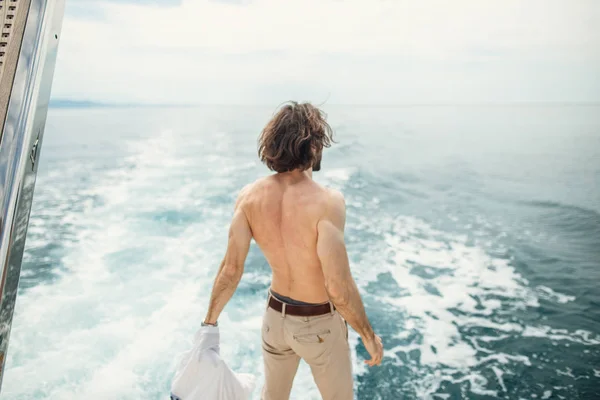 Rückansicht eines jungen Mannes, der am Rand der Jacht sitzt und aufs Meer blickt — Stockfoto