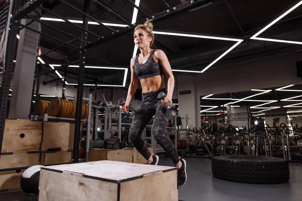 Rubia deportista activa está saltando sobre la caja en un gimnasio de entrenamiento cruzado — Foto de Stock