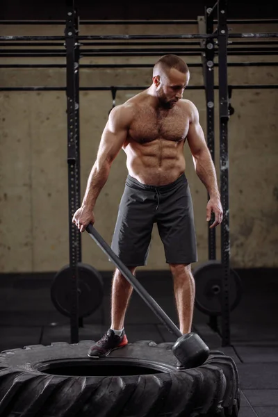 Guapo agradable ajuste hombre está entrenando con martillo y el neumático —  Fotos de Stock