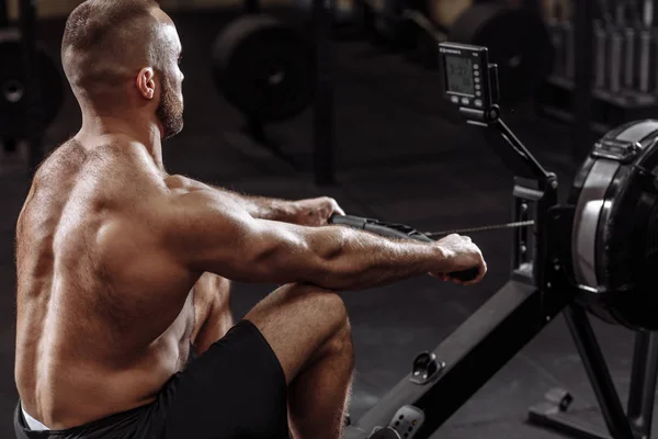 Side view photo of shirtles man using th rowing machine while training — Stock Photo, Image