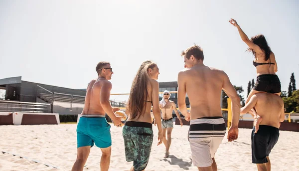 Group of friends walking on the beach volleyball court at sunny morning. — Stock Photo, Image