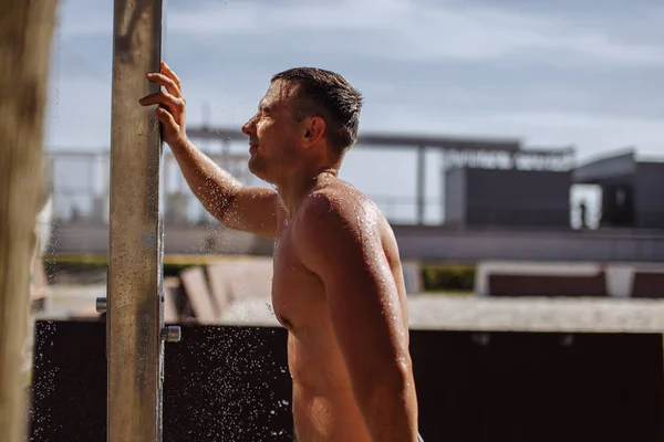 Bonito jovem topless caucasiano homem tomando um ao ar livre chuveiro no praia. — Fotografia de Stock