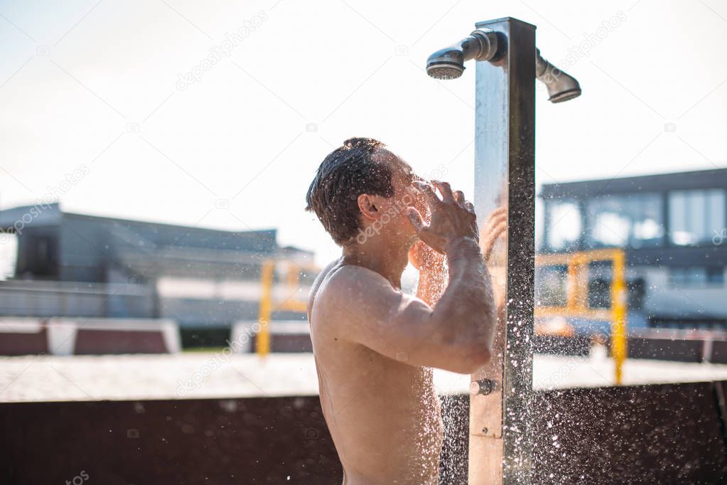 Young handsome caucasian muscular man, perfect body, taking outdoor shower after sunbathing. Summer holidays and vacation concept