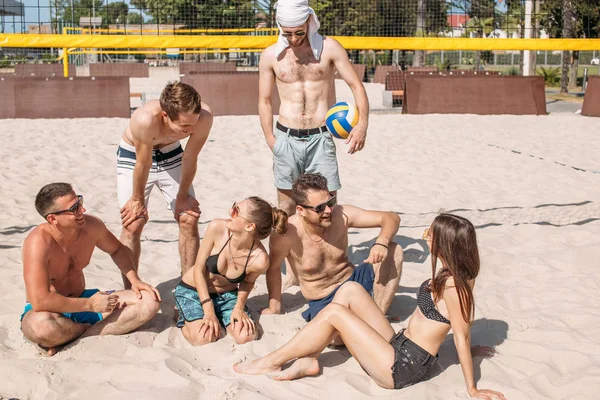 Grupa przyjaciół rasy kaukaskiej odpoczywa w odstępach czasu między setami na boisku plażowym. — Zdjęcie stockowe