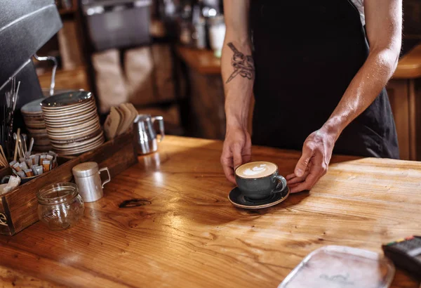 Een man is latte serveert op een houten tafel — Stockfoto