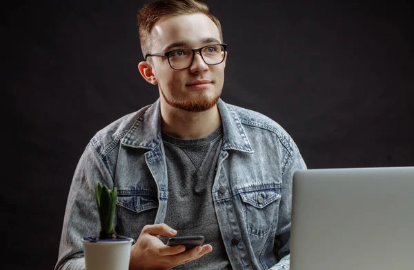 Aangename jonge zakenman zitten met mobiele telefoon in de voorkant van laptop — Stockfoto